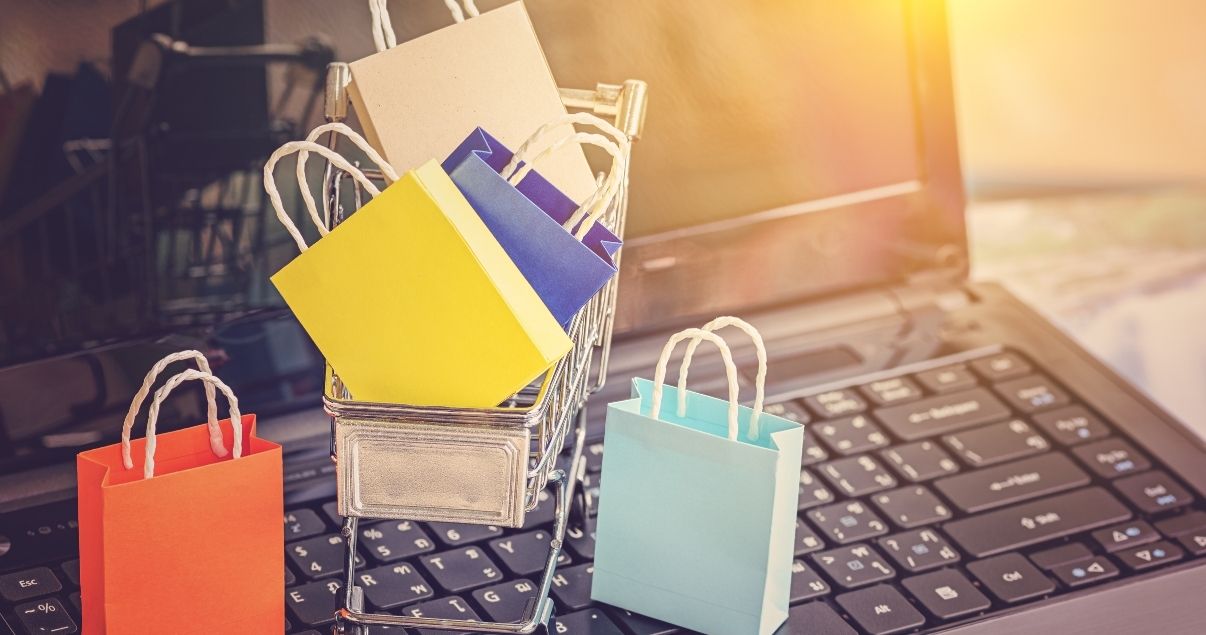 Bolsas y carrito de compras sobre computadora simbolizando las ventajas de tercerizar una solución de ecommerce